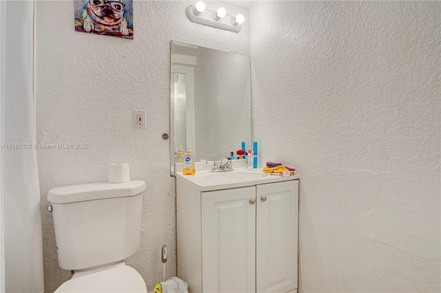 bathroom with toilet, vanity, and a textured wall