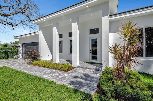 property entrance with stucco siding, decorative driveway, and a garage