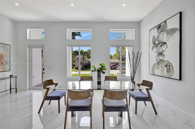 dining area featuring recessed lighting, baseboards, marble finish floor, and a towering ceiling