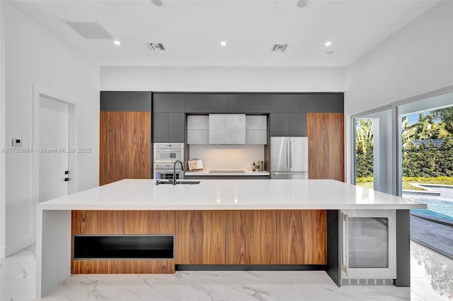 kitchen featuring modern cabinets, marble finish floor, freestanding refrigerator, light countertops, and a large island with sink