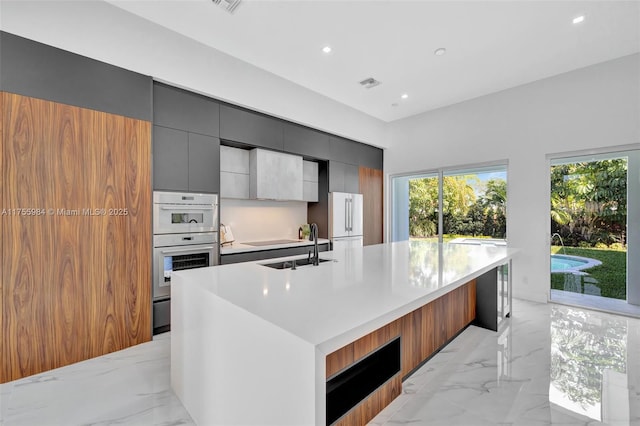 kitchen with modern cabinets, marble finish floor, a sink, white appliances, and a large island with sink