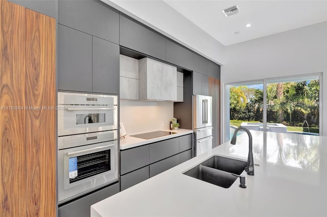 kitchen with a sink, black electric cooktop, gray cabinets, and light countertops