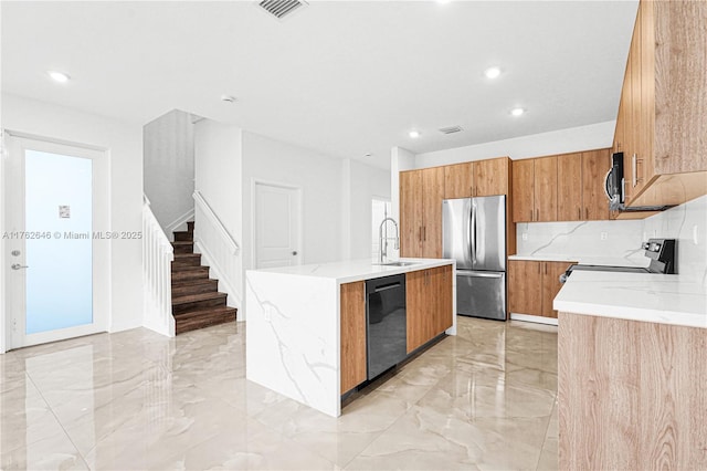 kitchen featuring a sink, brown cabinetry, marble finish floor, stainless steel appliances, and a kitchen island with sink