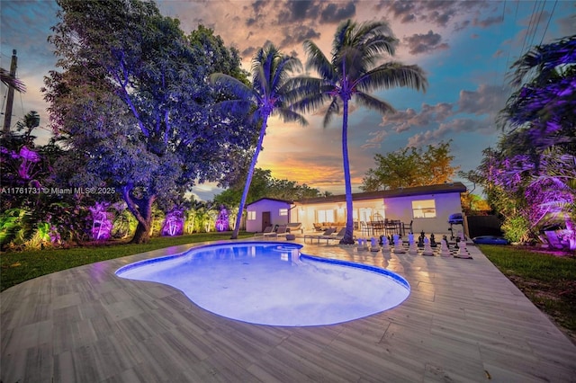 pool at dusk featuring an outbuilding, an outdoor pool, and a patio