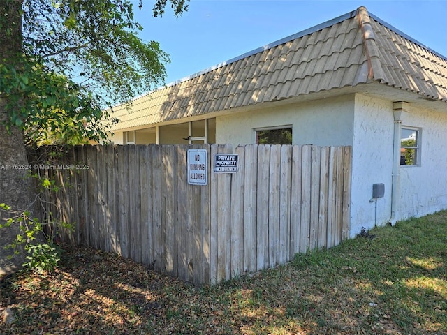 view of side of home with mansard roof, fence, and stucco siding