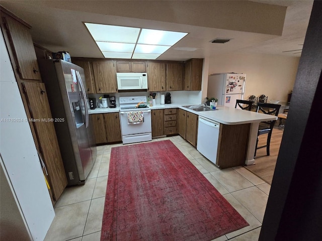 kitchen with white appliances, light tile patterned floors, visible vents, a peninsula, and a sink