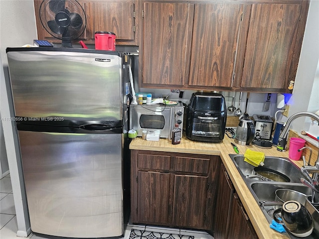 kitchen featuring a sink, dark brown cabinets, light countertops, and freestanding refrigerator