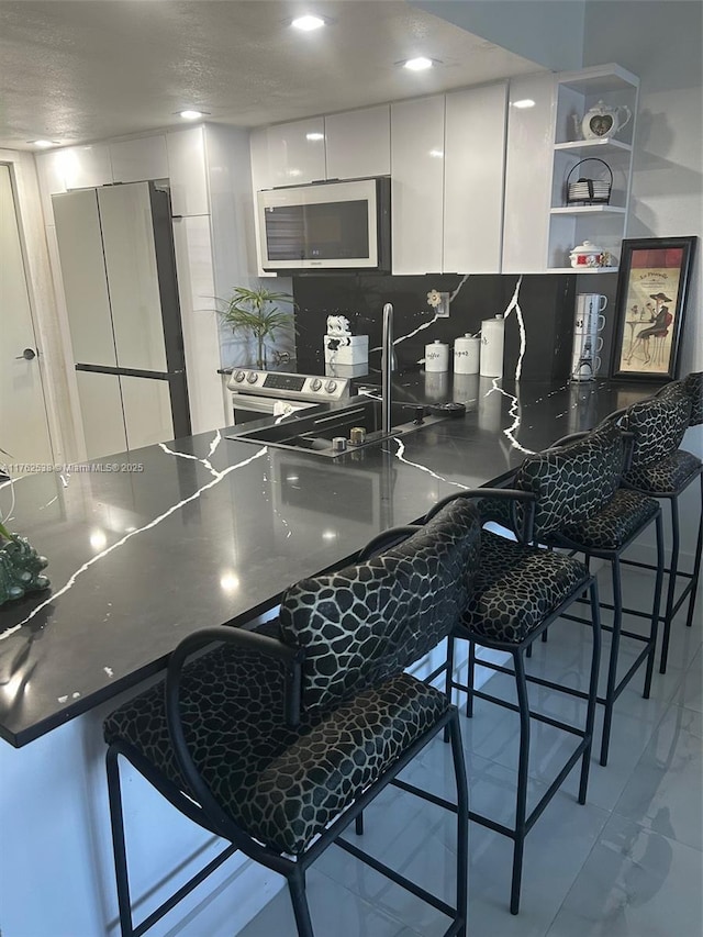 18555 NE 14th Ave Unit 609, Miami, FL 33179 - kitchen featuring white cabinetry, a kitchen bar, tasteful backsplash, a sink, and appliances with stainless steel finishes