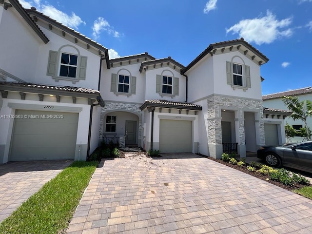 mediterranean / spanish house with an attached garage, stucco siding, stone siding, a tiled roof, and decorative driveway