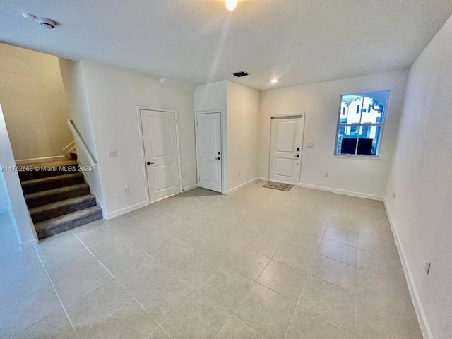 unfurnished living room with stairway, light tile patterned floors, baseboards, and visible vents