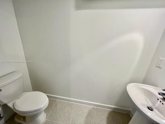 half bathroom featuring tile patterned floors, toilet, baseboards, and a sink