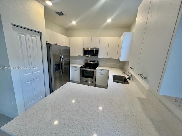 kitchen featuring visible vents, light stone countertops, appliances with stainless steel finishes, a peninsula, and a sink