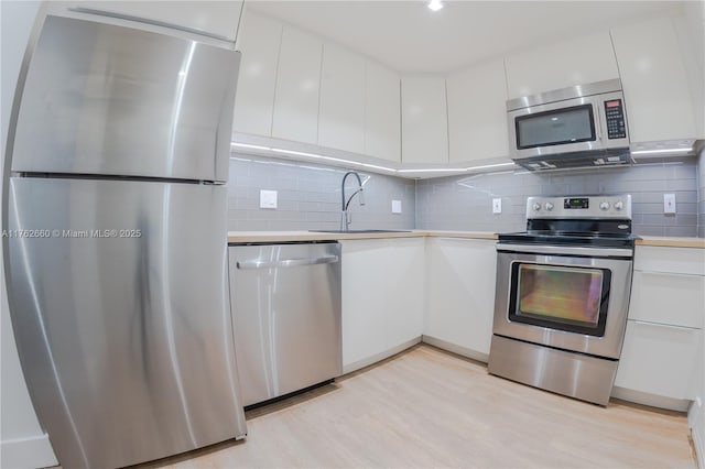 kitchen featuring light countertops, light wood-style floors, white cabinets, stainless steel appliances, and a sink