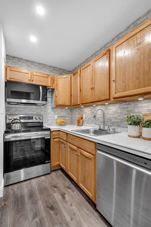 kitchen featuring light wood-type flooring, light countertops, decorative backsplash, appliances with stainless steel finishes, and a sink