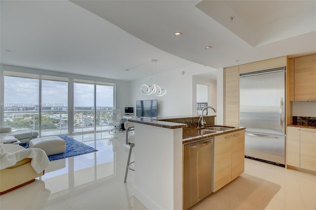 kitchen featuring dark stone countertops, a kitchen island with sink, a sink, stainless steel appliances, and decorative light fixtures