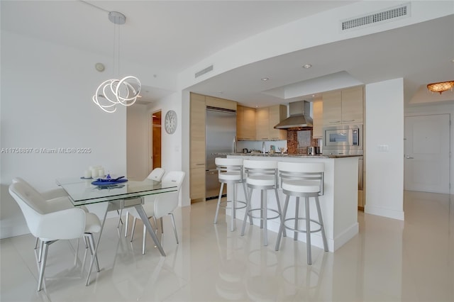 kitchen with visible vents, built in appliances, a kitchen bar, modern cabinets, and wall chimney exhaust hood