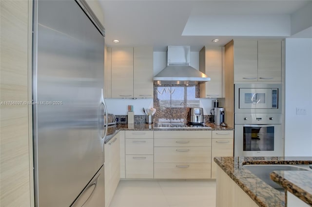 kitchen with modern cabinets, dark stone countertops, recessed lighting, appliances with stainless steel finishes, and wall chimney range hood