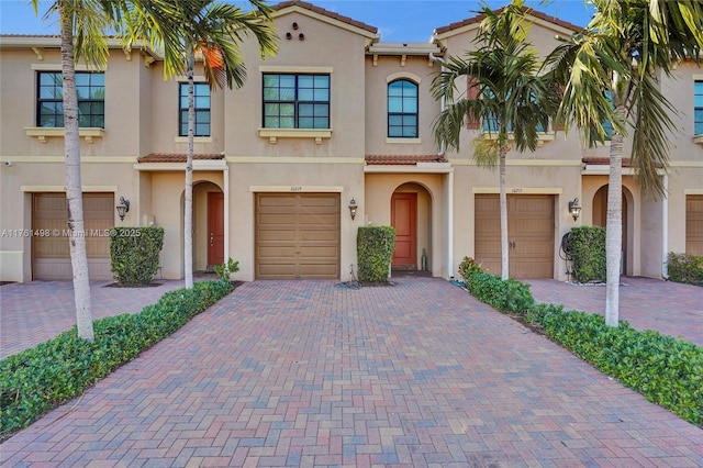 townhome / multi-family property featuring a tiled roof, stucco siding, driveway, and a garage