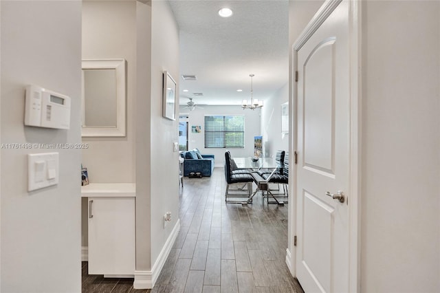 corridor with wood finished floors, baseboards, recessed lighting, a textured ceiling, and a chandelier