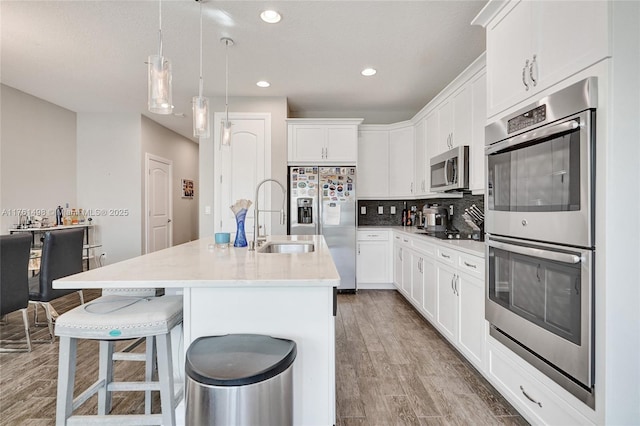 kitchen featuring a sink, light wood-type flooring, decorative backsplash, appliances with stainless steel finishes, and a kitchen island with sink