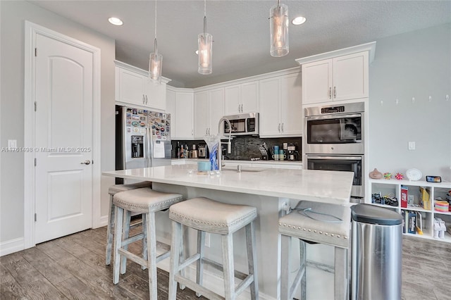 kitchen with light wood finished floors, white cabinetry, stainless steel appliances, light countertops, and decorative backsplash