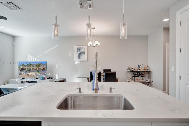 kitchen with hanging light fixtures, visible vents, light stone counters, and a sink