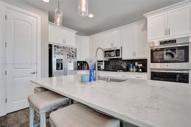 kitchen featuring stainless steel appliances, white cabinets, light stone countertops, dark wood-style flooring, and hanging light fixtures