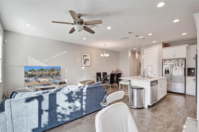 living area featuring visible vents, light wood finished floors, recessed lighting, a textured ceiling, and ceiling fan with notable chandelier