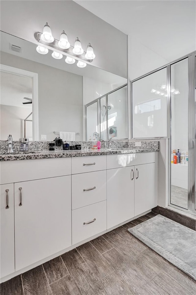 full bathroom with visible vents, wood tiled floor, double vanity, a sink, and a shower stall