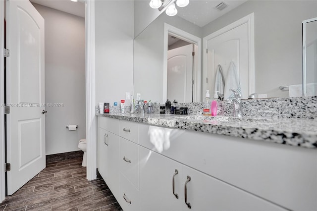 bathroom with wood finish floors, visible vents, toilet, and vanity