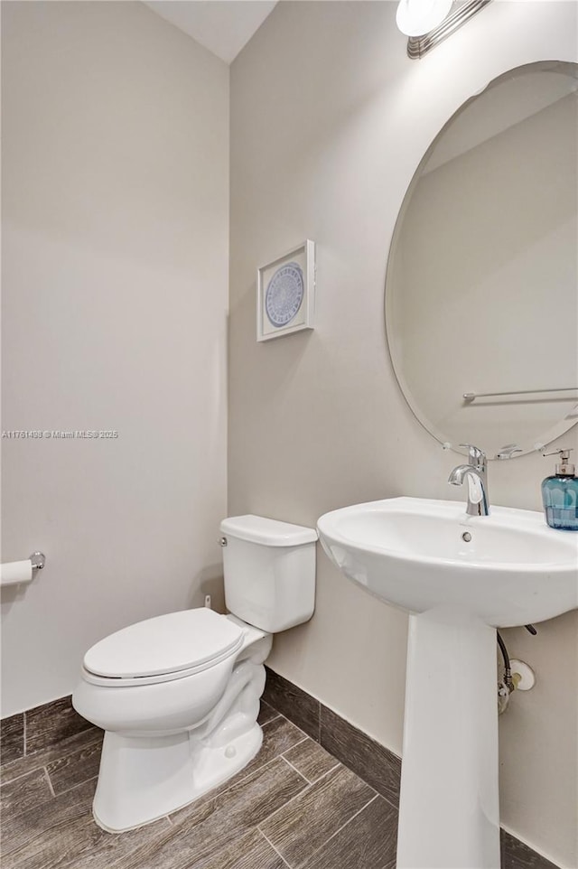 half bath featuring a sink, baseboards, toilet, and wood tiled floor