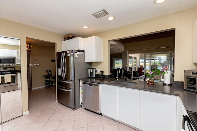 kitchen with a sink, stainless steel appliances, dark countertops, and white cabinetry