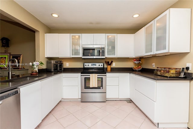 kitchen featuring dark countertops, white cabinetry, stainless steel appliances, and a sink