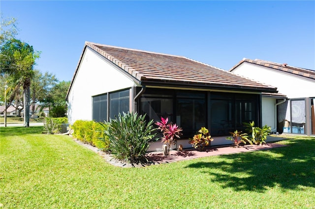 rear view of property featuring a yard, stucco siding, a tiled roof, and a sunroom
