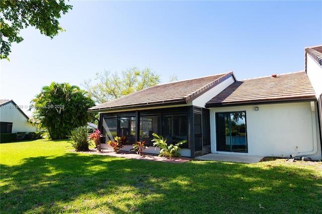 rear view of house featuring a sunroom, a tiled roof, stucco siding, and a lawn