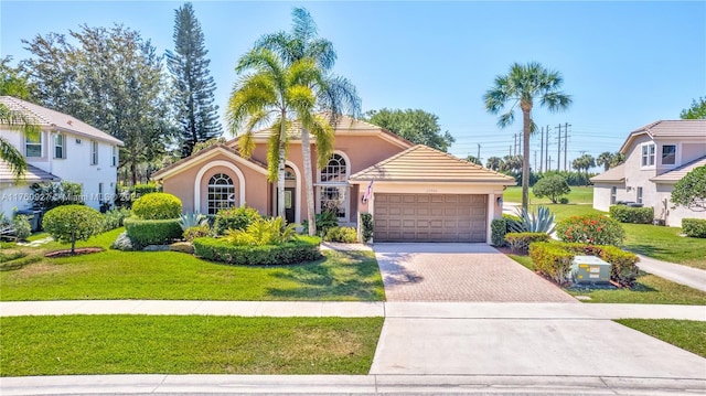 mediterranean / spanish home with a garage, decorative driveway, a front lawn, and stucco siding