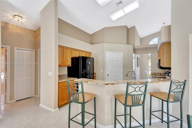 kitchen featuring electric range, visible vents, black fridge with ice dispenser, a peninsula, and a breakfast bar area