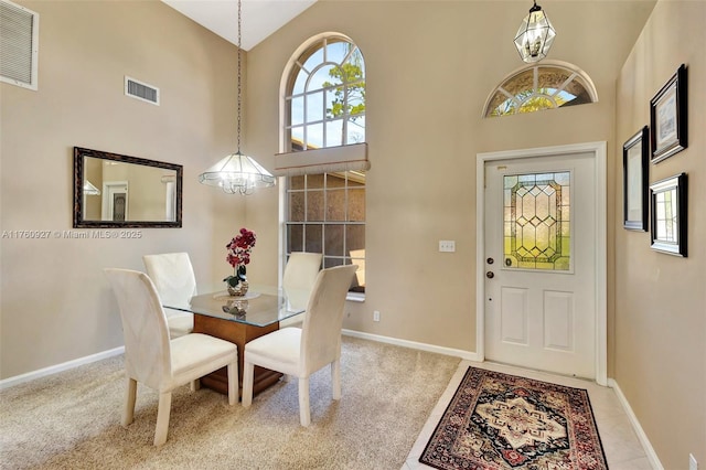 carpeted dining area with visible vents, baseboards, a notable chandelier, and a high ceiling