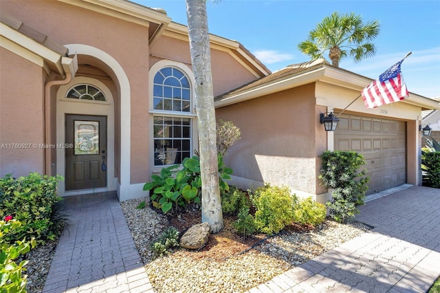 view of exterior entry with a garage, driveway, and stucco siding