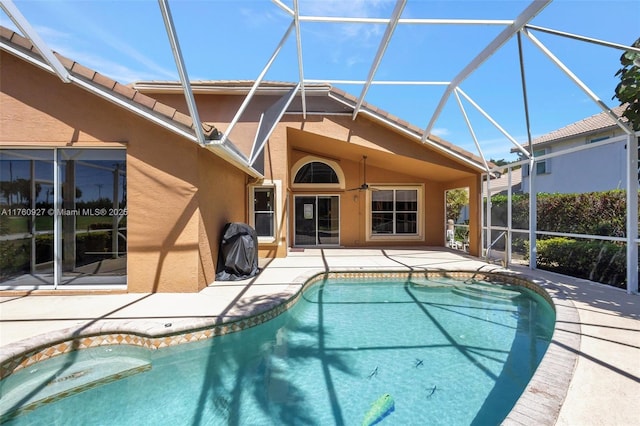 outdoor pool featuring glass enclosure, a ceiling fan, and a patio