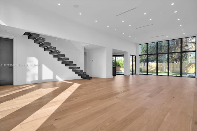 unfurnished living room featuring a wall of windows, light wood-type flooring, recessed lighting, and stairs