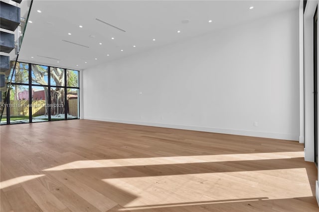 empty room with recessed lighting, a wall of windows, baseboards, and wood finished floors