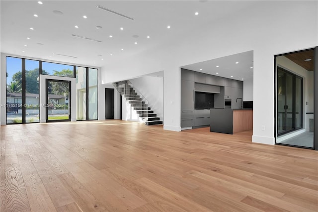 unfurnished living room featuring expansive windows, light wood finished floors, baseboards, and stairway
