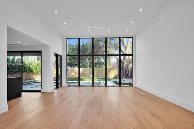 empty room with light wood finished floors, floor to ceiling windows, a wealth of natural light, and baseboards