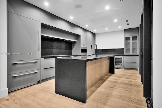 kitchen with beverage cooler, light wood-style flooring, modern cabinets, and dark countertops