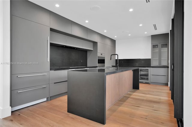 kitchen with dark countertops, oven, beverage cooler, light wood-style floors, and modern cabinets