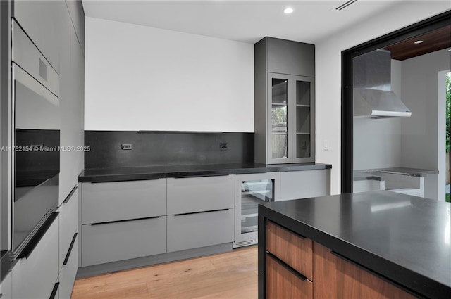 kitchen with beverage cooler, modern cabinets, dark countertops, and light wood-style floors