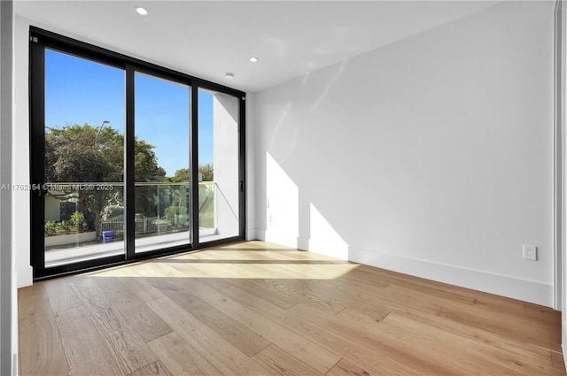 unfurnished room featuring a wall of windows, recessed lighting, wood finished floors, and baseboards