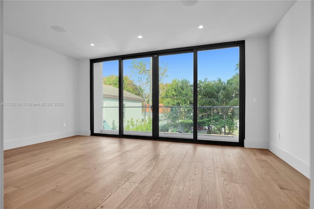 unfurnished room featuring a wall of windows, wood finished floors, and baseboards