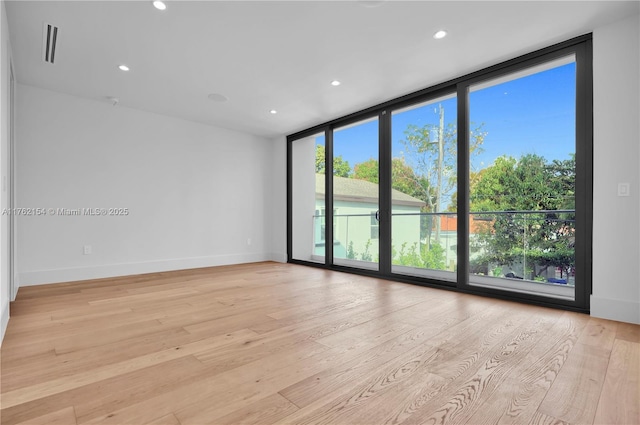 empty room with recessed lighting, baseboards, floor to ceiling windows, and light wood finished floors